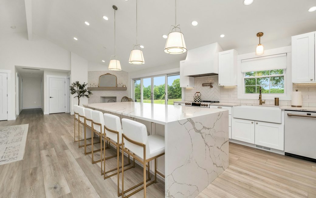 A bright kitchen with a marble island, bar stools and pendant lights
