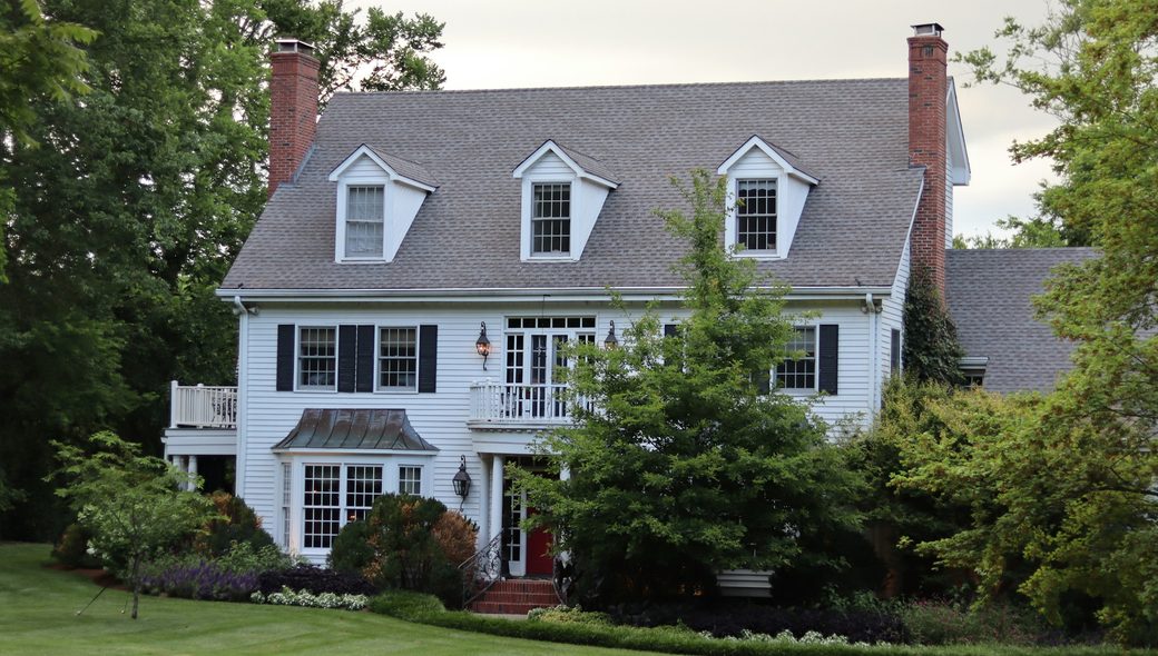 A white colonial house with black shutters and brick chimneys behind a green lawn
