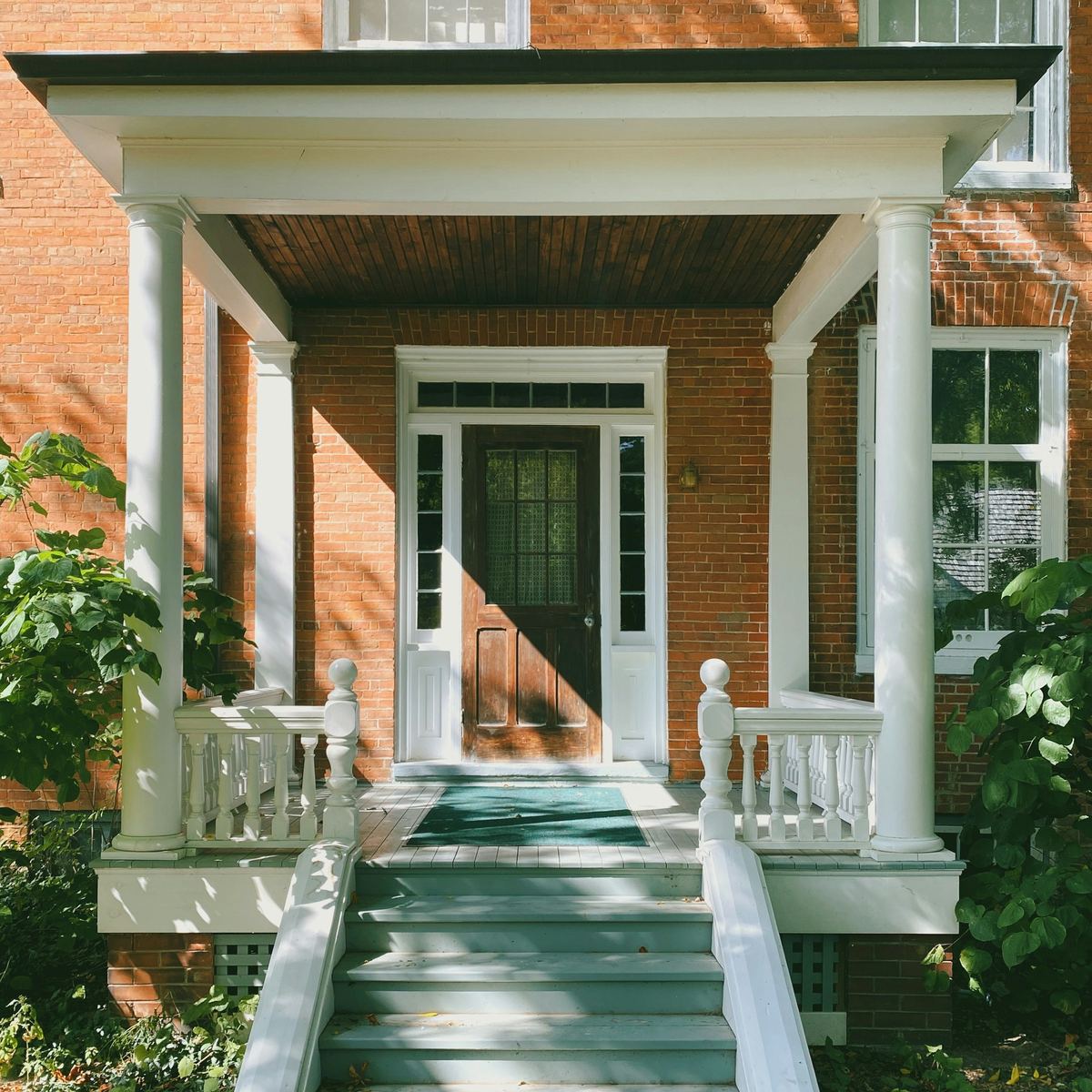 A brick two-storey house with a white covered porch and steps