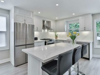 A white kitchen with a quartz island and a window over the sink
