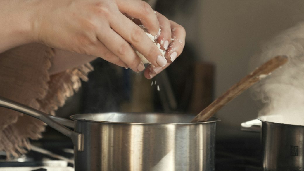 Hands adding salt to a pot on the stove