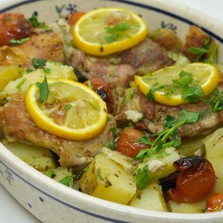 Roasted chicken with charred lemon and potatoes in a ceramic dish