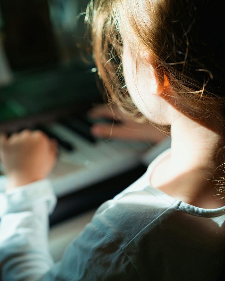 A young girl playing the piano in soft window light