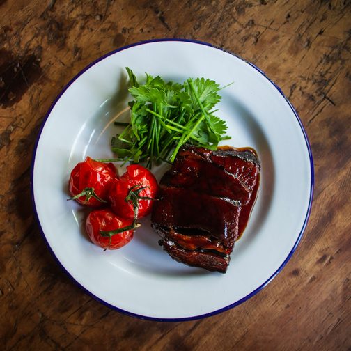 Braised short rib with roasted tomatoes on an enamel plate