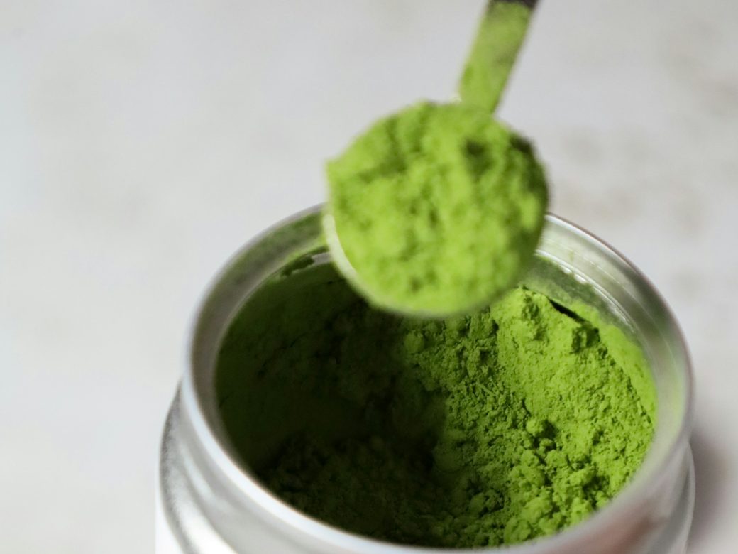 A scoop of bright green powder lifted from an open tin