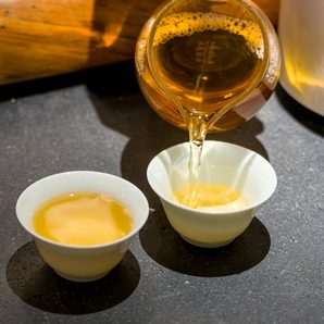 Golden tea poured from a glass pitcher into small white cups