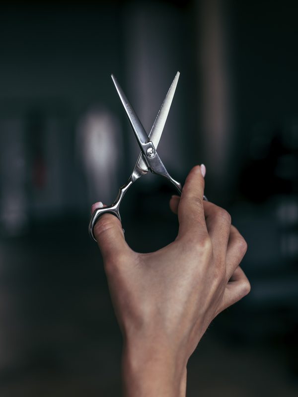 A hand holding open hair-cutting shears against a dark studio