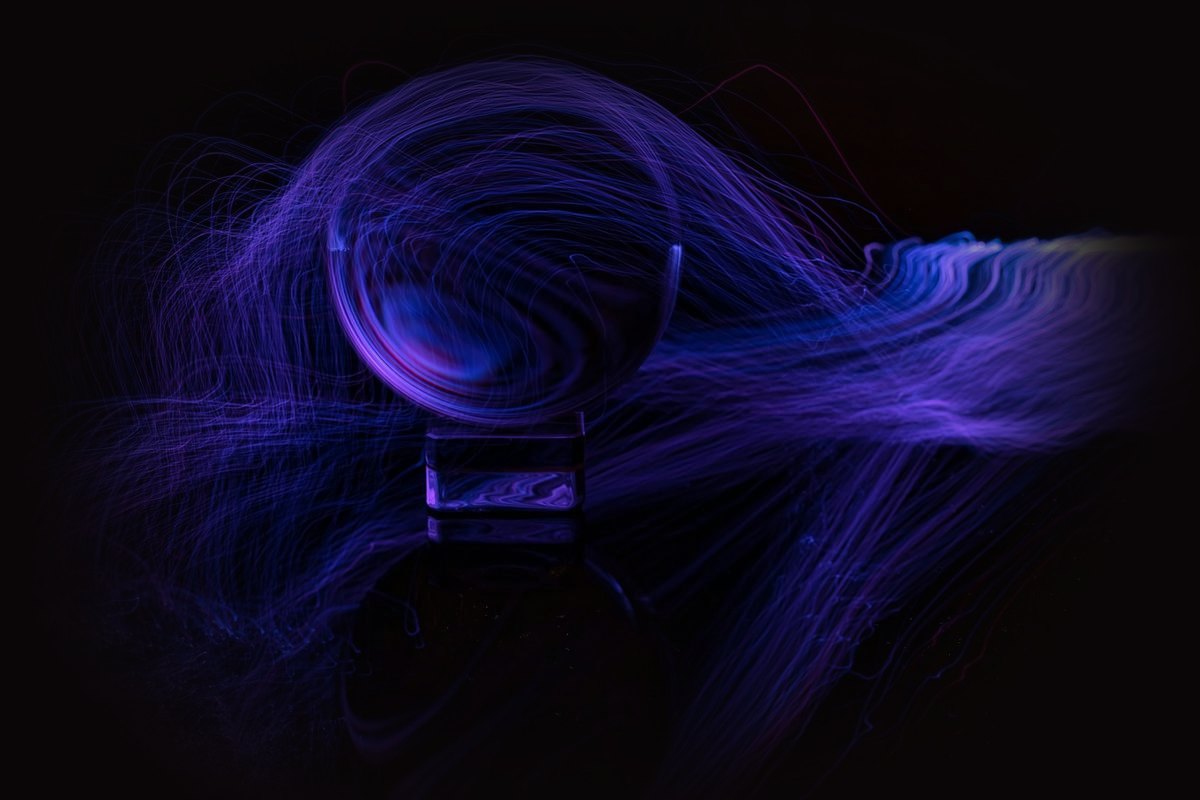 Violet light trails circling a glass sphere in the dark