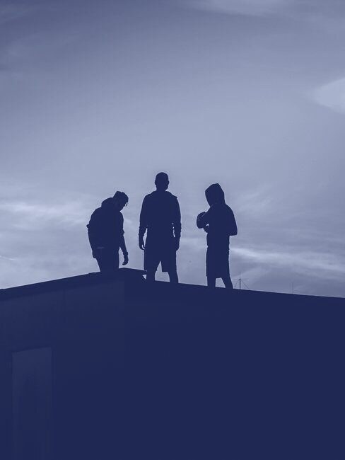 Three crew members silhouetted on a rooftop at dusk