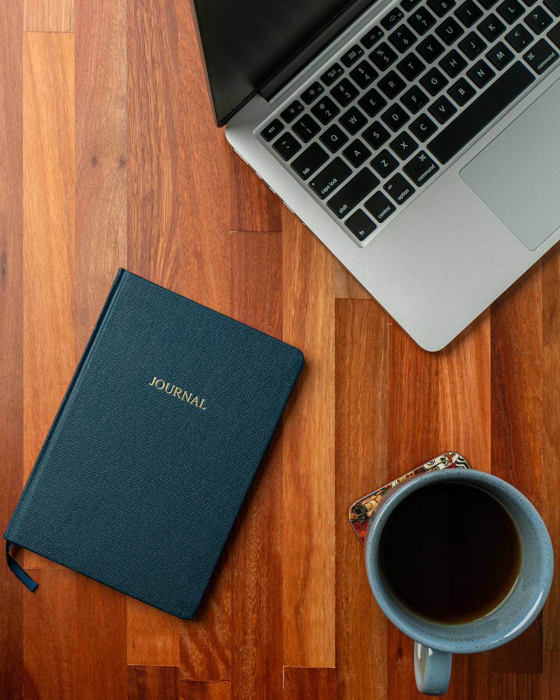 A journal, laptop and cup of black coffee on a wooden floor, seen from above