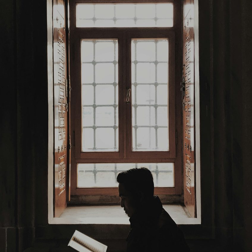A person reading by a window in evening light