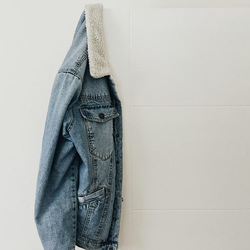 A light-wash denim jacket hanging on a white door