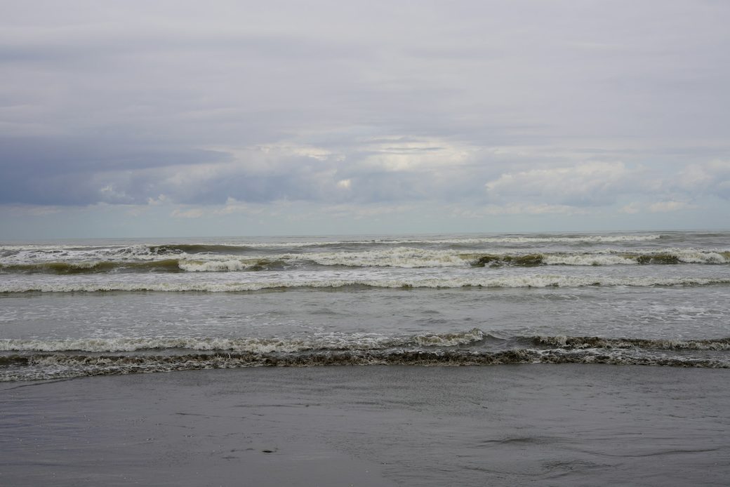 Low waves rolling onto a wide sandy beach under soft cloud