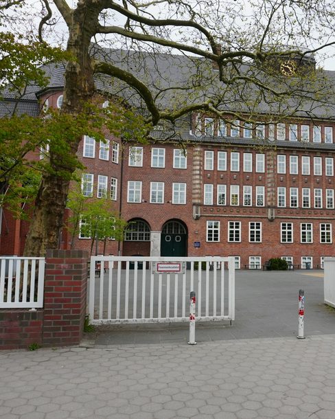 A red-brick school building with arched doors behind an open gate