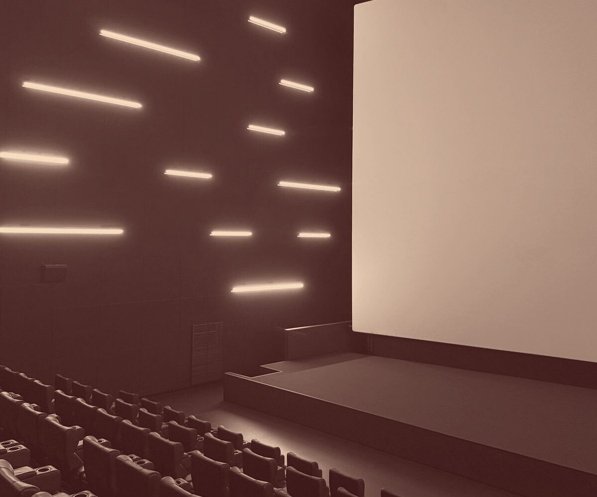 An empty cinema with rows of seats facing a lit screen