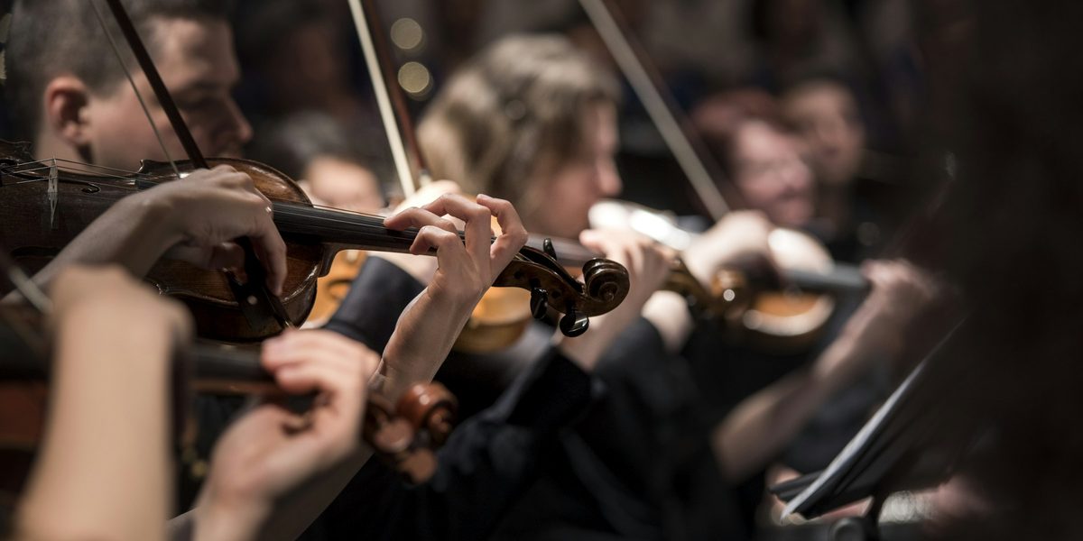 Violinists playing in a row, bows raised, in warm stage light