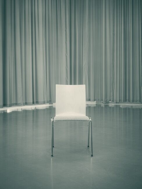 A single chair on an empty stage in front of a curtain