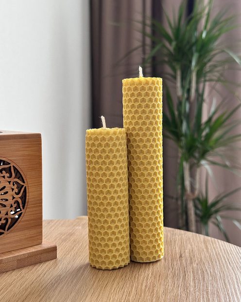 Two hand-rolled beeswax candles on a wooden table