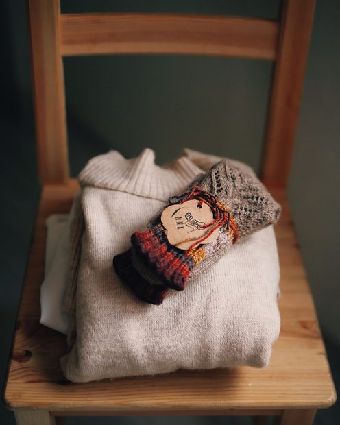 Thick knitted wool socks folded on a cream sweater on a wooden chair