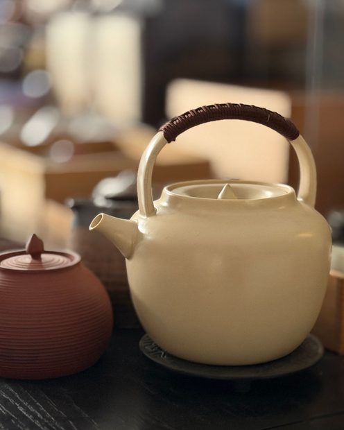 A cream stoneware teapot beside a small clay pot