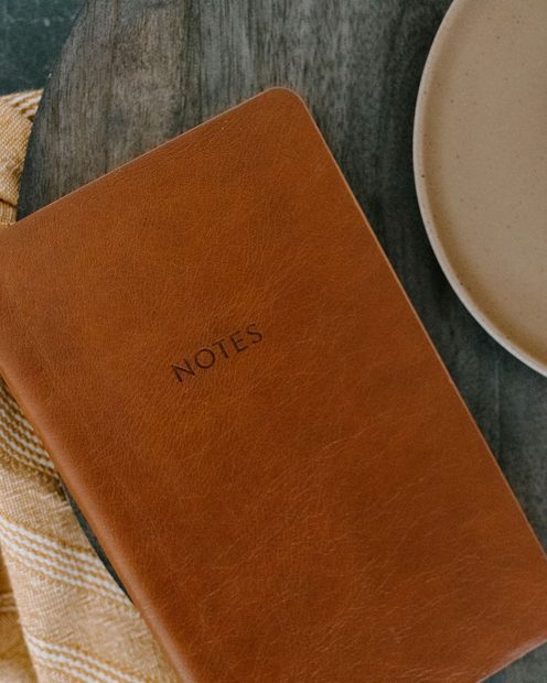 A tan leather notebook on a linen cloth next to a cup of coffee