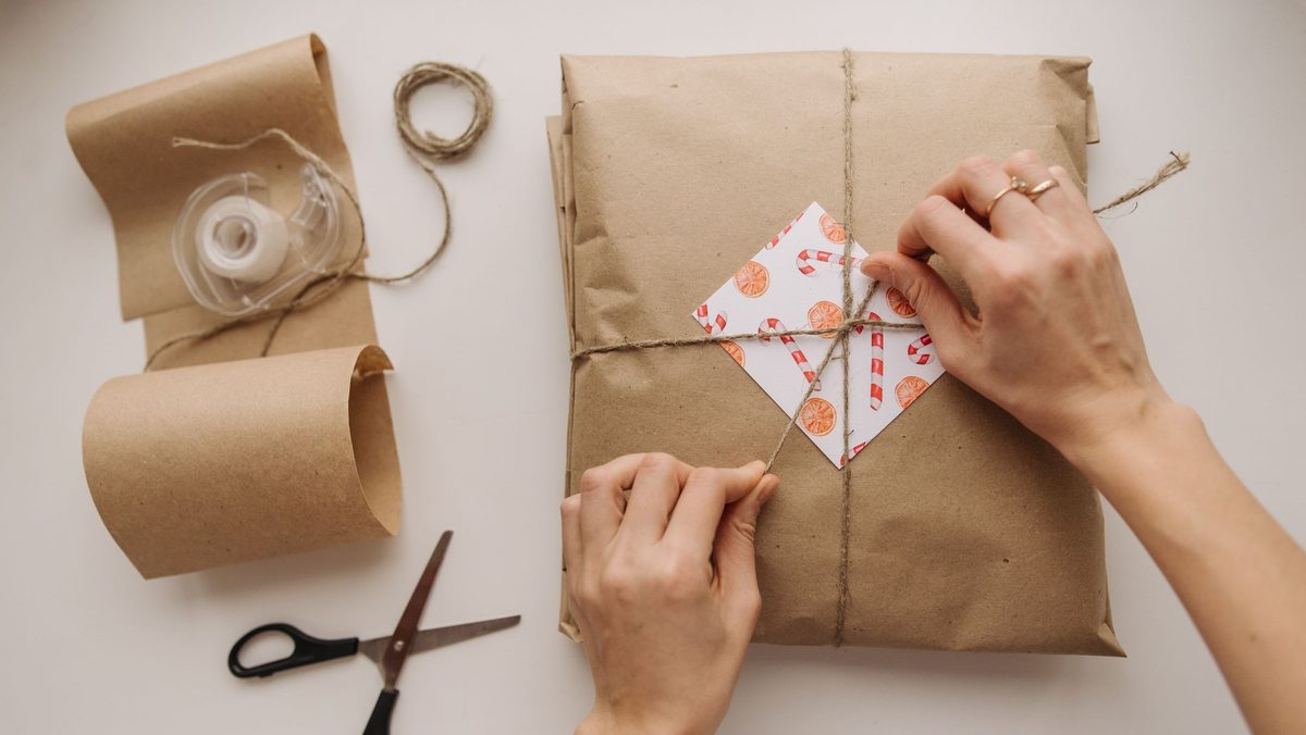 Hands tying string around a parcel wrapped in brown paper