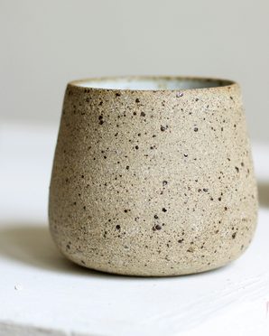 A speckled stoneware cup on a white plinth