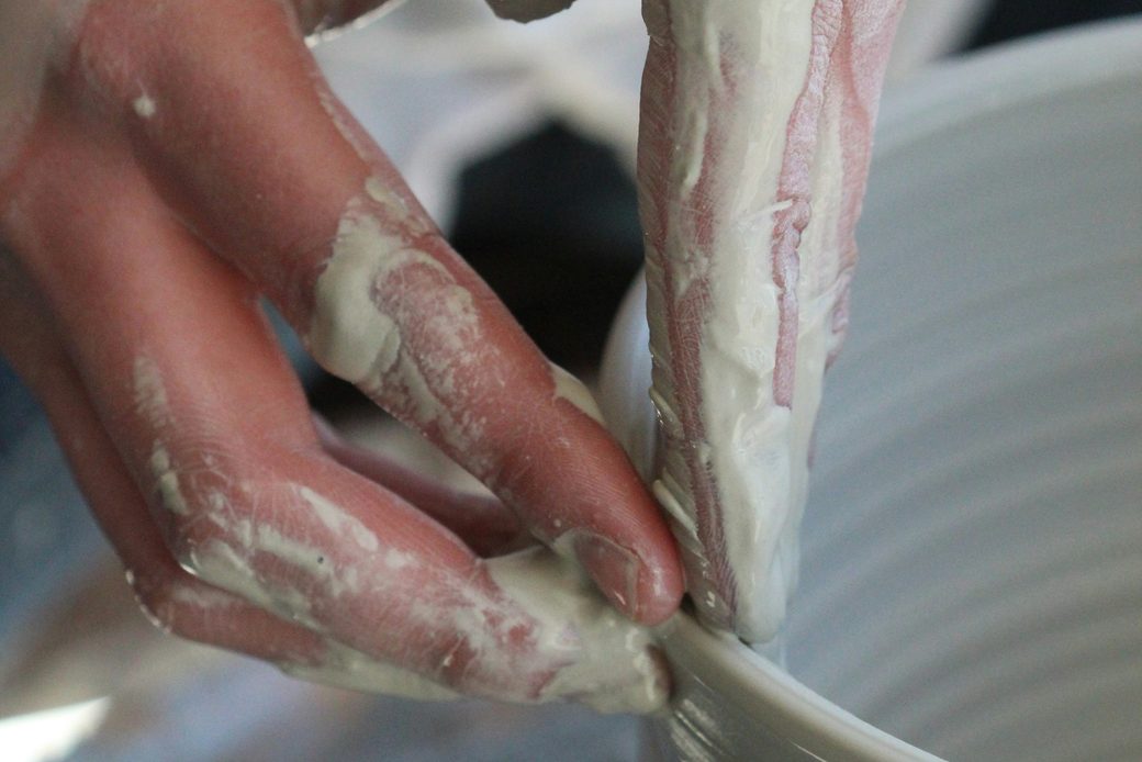 Clay-covered hands shaping the rim of a bowl on a wheel