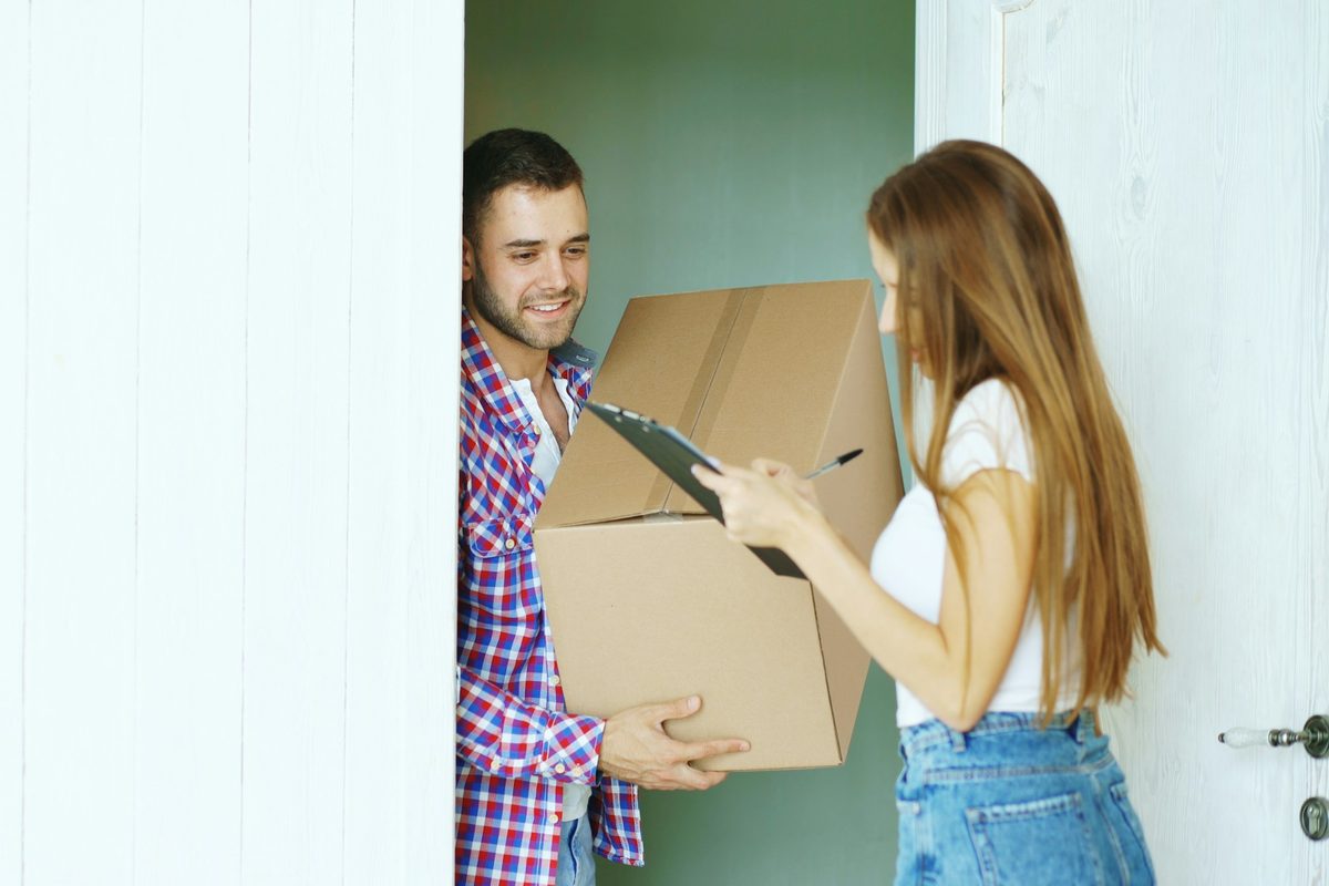 A courier handing a cardboard box to a woman at her front door