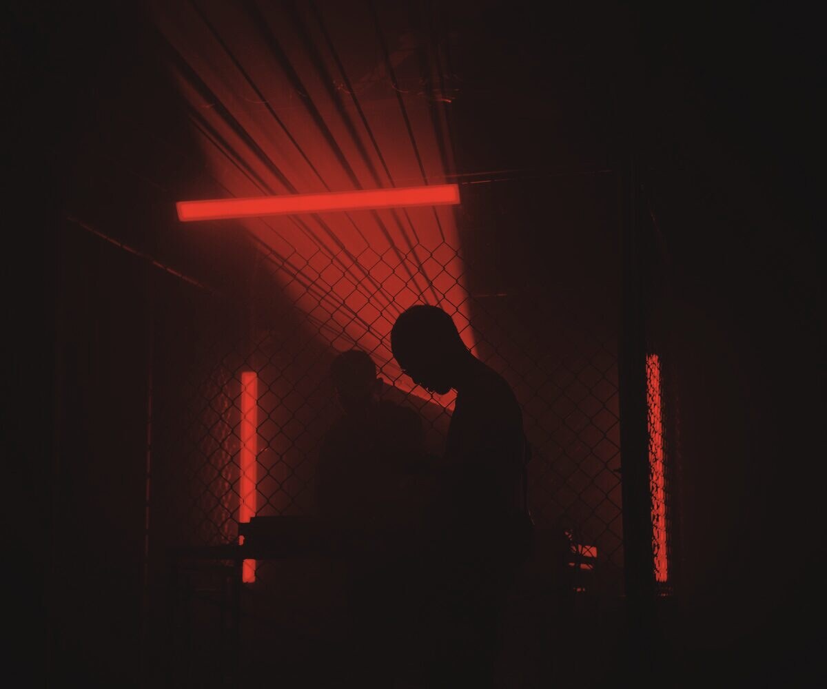 Two band members in silhouette against a lit fence in a dark room