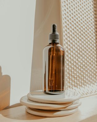 An amber glass dropper bottle of serum on stacked stone coasters
