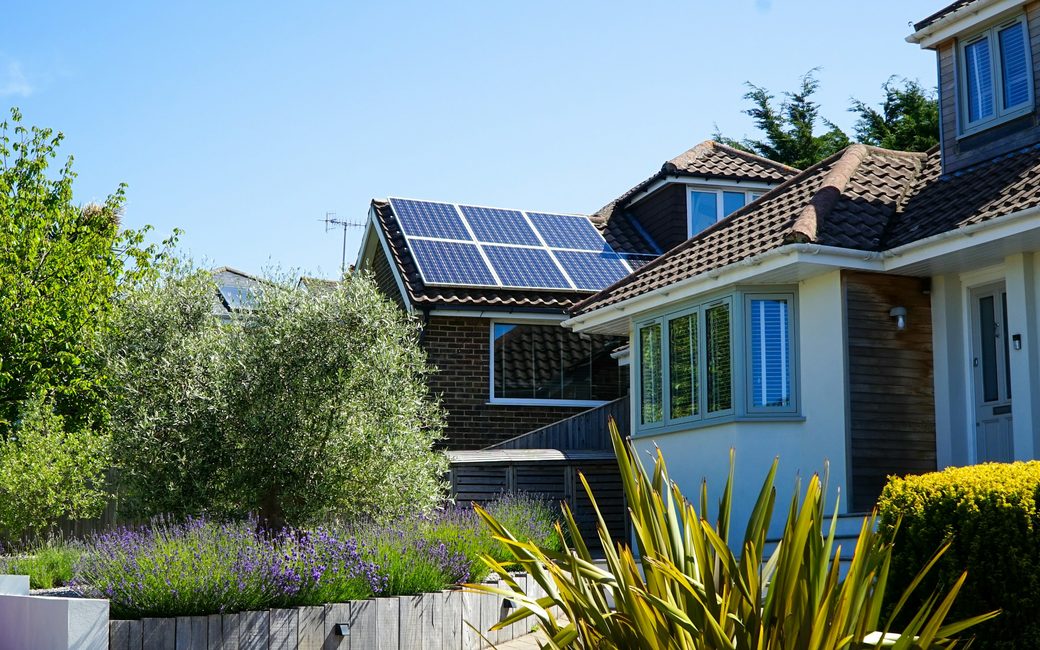 A two-storey house with solar panels on the roof and a summer garden