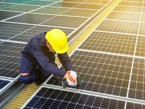 An installer in a hard hat securing solar panels