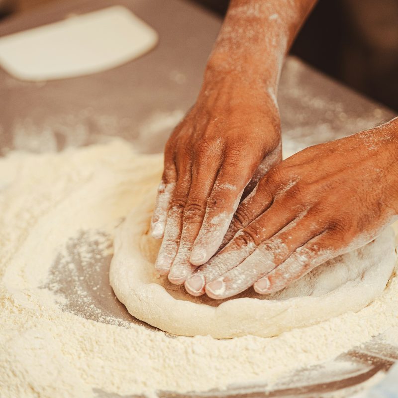 Floury hands pressing a round of dough on a counter