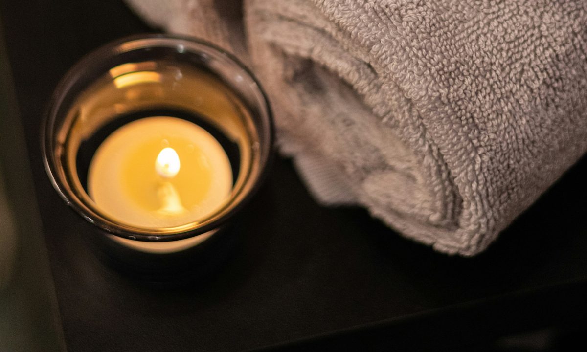 A rolled towel beside a lit tealight in a glass holder