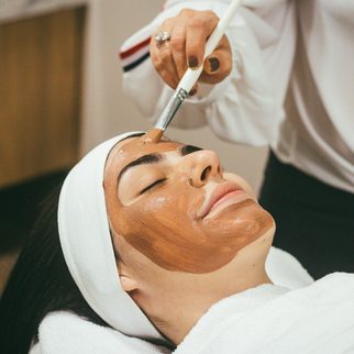 An esthetician brushing a clay mask onto a client's face