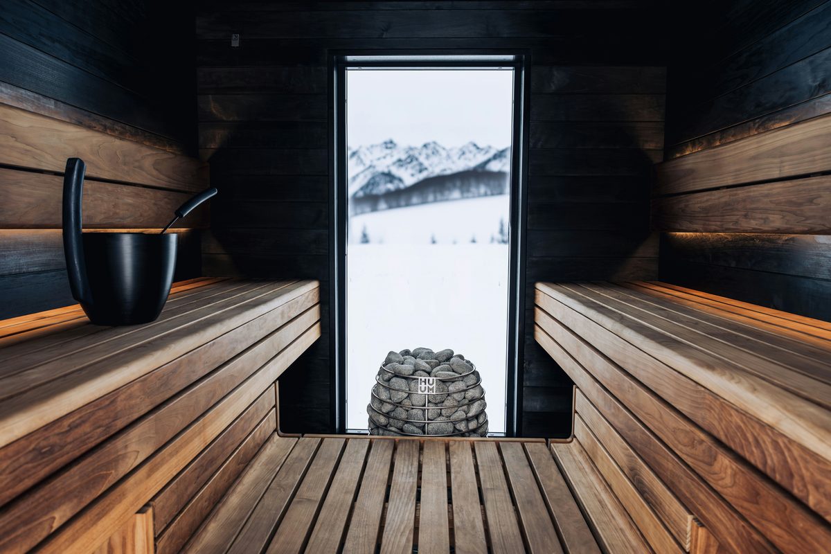 A dark wooden sauna with a tall window onto snowy mountains
