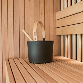 A black sauna bucket and ladle on a pale wooden bench