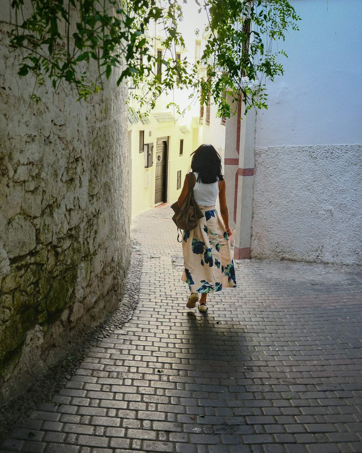 A woman in a light summer dress walking down a sunlit cobbled alley