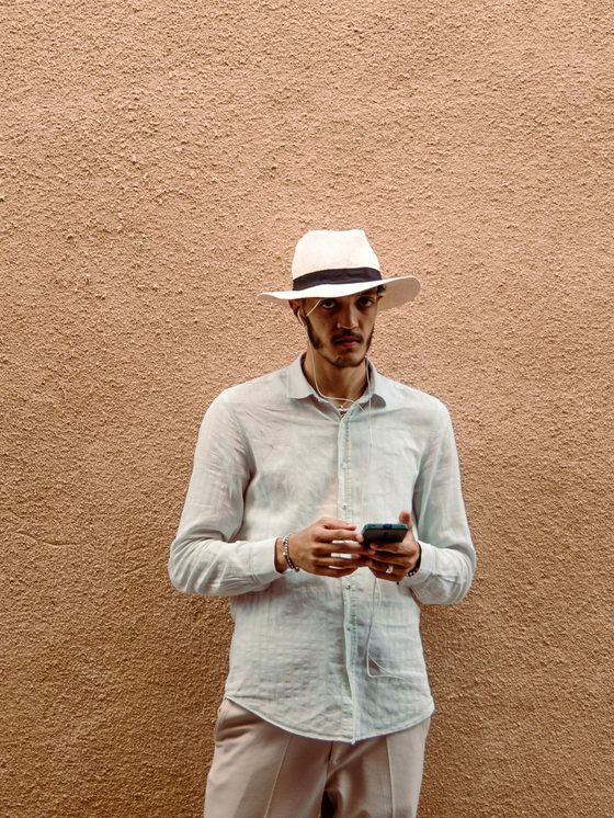 A man in a linen shirt and hat against a terracotta wall