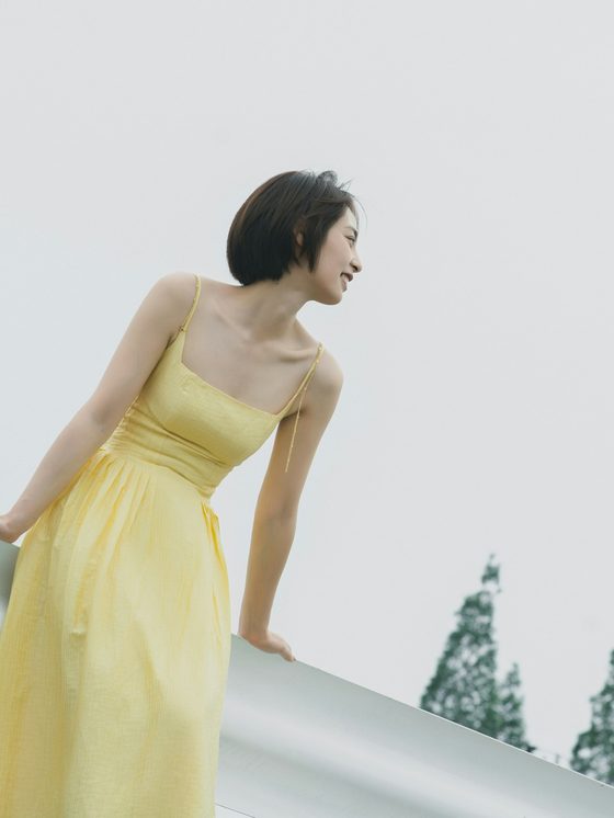 A woman in a pale yellow slip dress leaning on a white rail