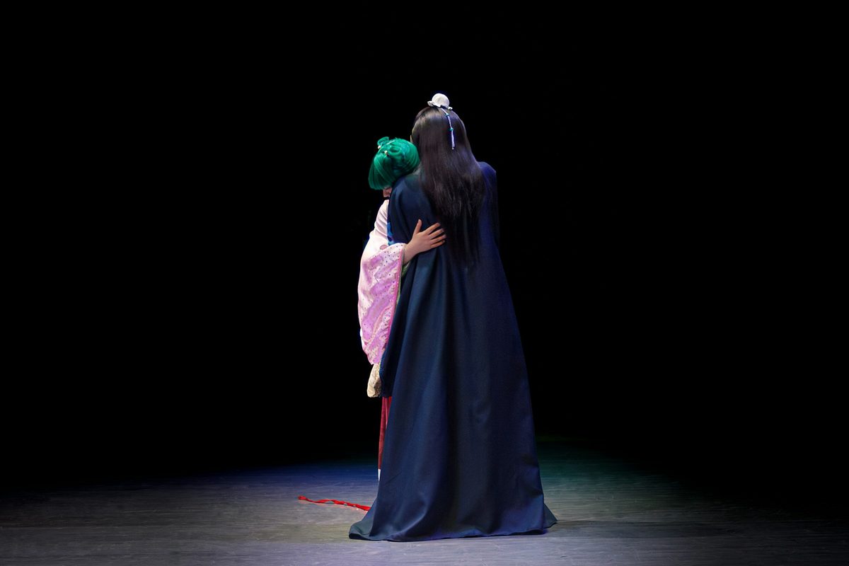 An actor in costume alone in a spotlight on a dark stage