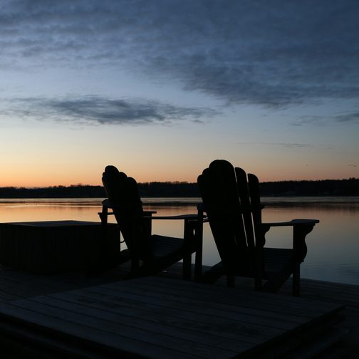 Two chairs on a lakeside dock at dusk