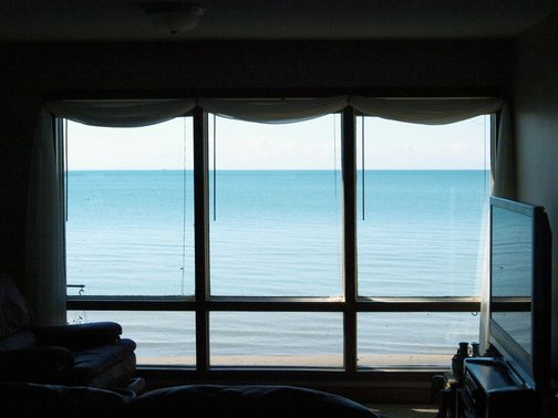 A dark room with wide windows onto a blue sea