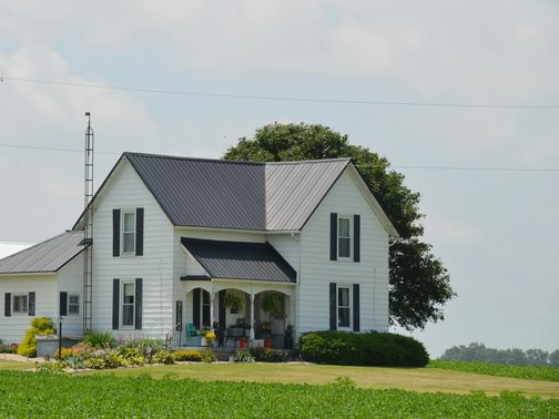 A white farmhouse with a porch beside a big tree