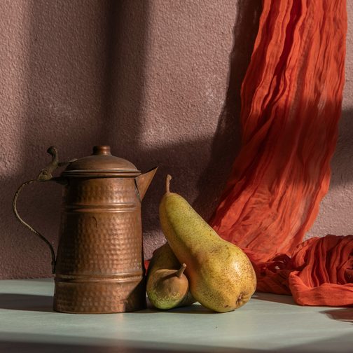 A copper jug, two pears and a red cloth on a table