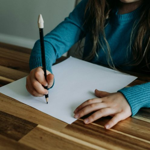 A child's hands writing on paper with a pencil