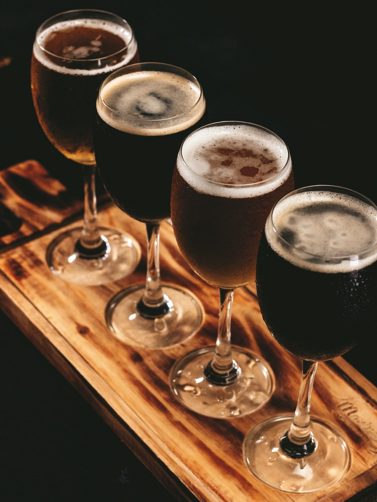 A flight of four dark beers on a wooden paddle
