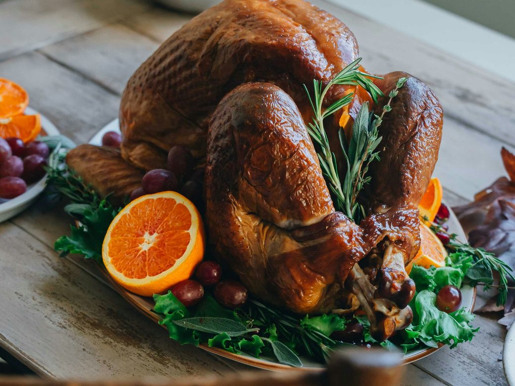A golden roast turkey garnished with oranges and rosemary on a wooden table