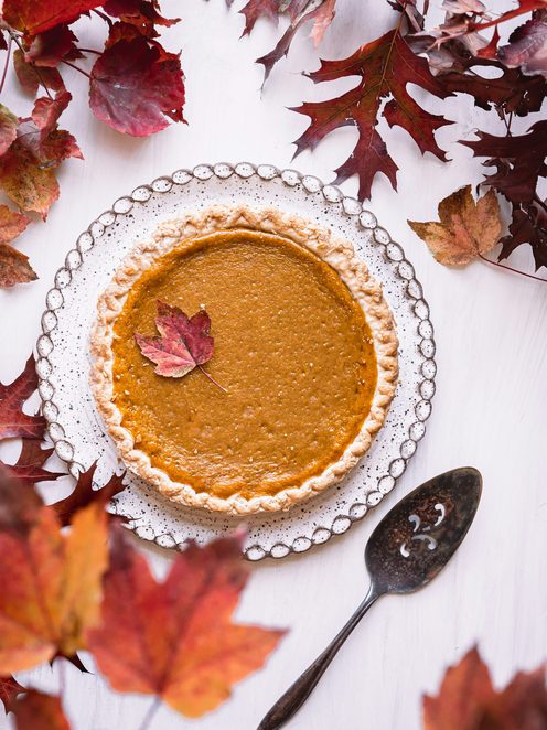 A pumpkin pie in a fluted dish surrounded by autumn leaves